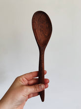 Load image into Gallery viewer, A rich red wooden handcarved cooking spoon held up against a white wall