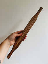 Load image into Gallery viewer, A hand holds an oak wood rolling pin against a cream wall
