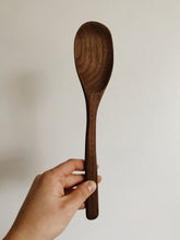 Load image into Gallery viewer, A dark brown wooden handcarved cooking spoon held up against a white wall - Miscellany and Co.