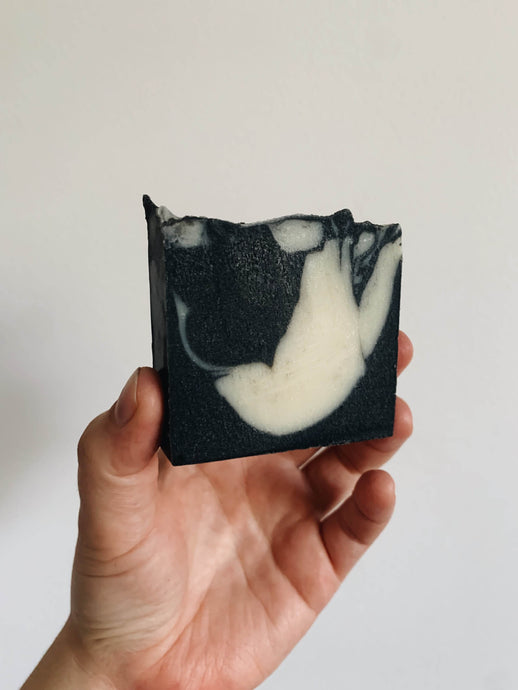 A black and white swirled square soap bar held in Kitty's hand against a white wall