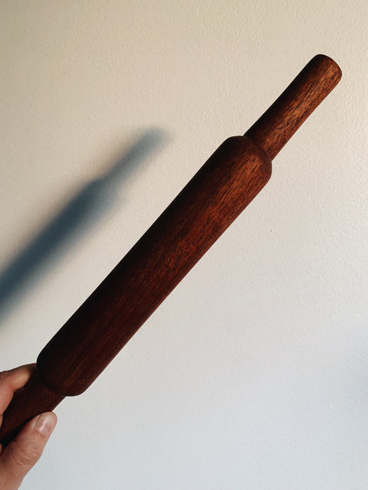 French Rolling Pin in a rich brown wood held up against a white wall