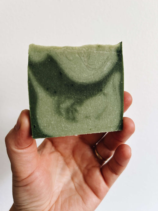 Hand holding a soap swirled in light and dark green against a white background