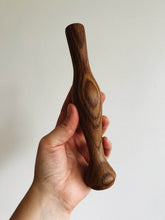 Load image into Gallery viewer, A hand holds an oak wood cocktail muddler against a cream wall