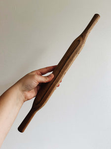 A hand holds an oak wood rolling pin against a cream wall