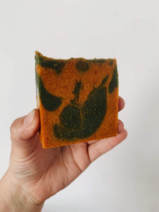 A green and orange swirled soap bar held up against a white wall