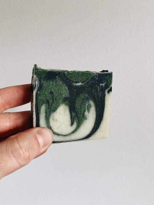 A green, black and cream swirled soap bar held up against a white wall
