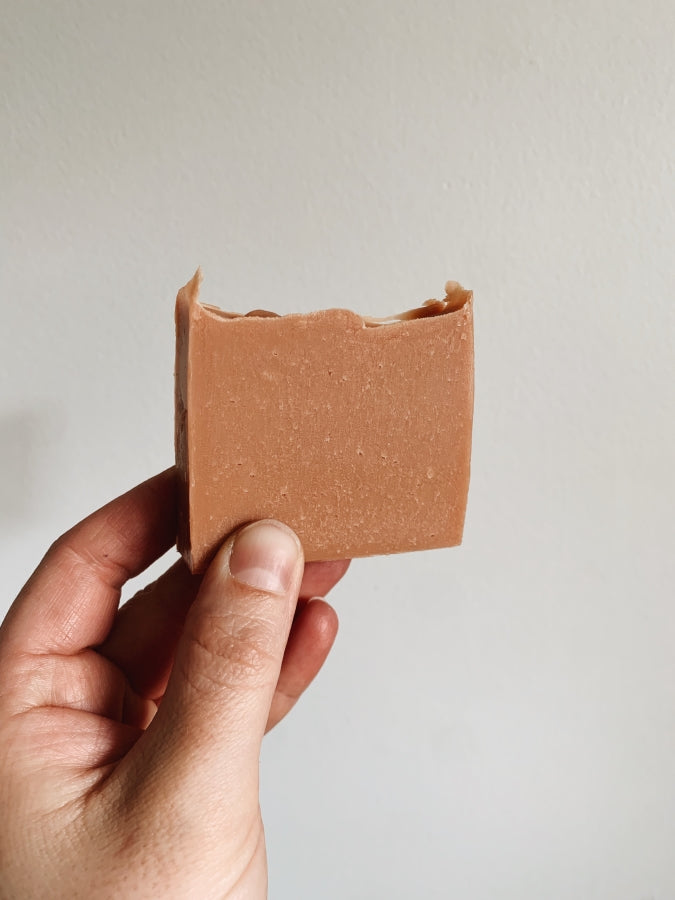 Peachy soap bar held up against a white wall