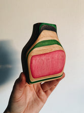 Load image into Gallery viewer, Vase made out of recycled skateboards held up against a white wall - pink, green, maple , and black ply layers